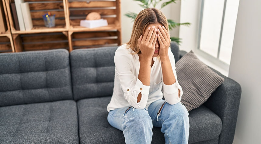 Frau mit Stimmungsschwankungen sitzt auf einem Sofa und hält ihre Hände vors Gesicht
