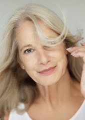 Frau mittleren Alters mit einem sanften Lächeln und graublonden Haaren, die ihr um das Gesicht wehen