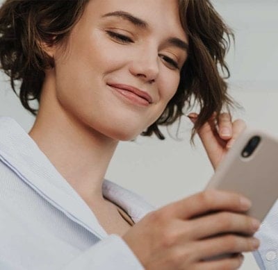 Person in weißem Hemd hält ein Smartphone in der Hand und berührt mit der anderen Hand eine Haarsträhne.