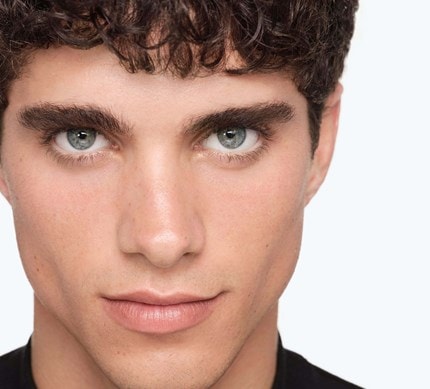 Nahaufnahme des Gesichts eines jungen Mannes mit dunklen Haaren und hellen Augen