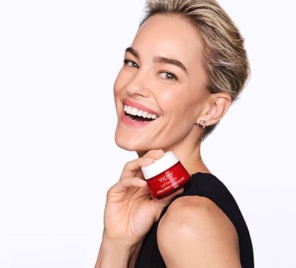 Seitenprofil einer lächelnden Frau mit kurzen Haaren welche Vichy Creme in der Hand hält