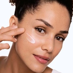 Frau verteilt Sonnencreme auf ihrer Wange