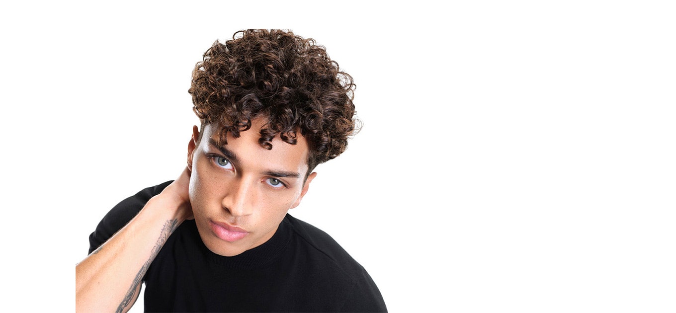 Männliches Model mit braunen Locken schaut frontal und greift sich in den Nacken