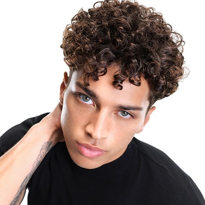 Männliches Model mit braunen Locken schaut frontal und greift sich in den Nacken