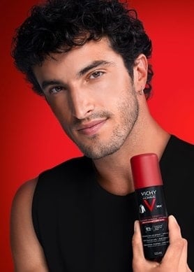 Mann hält Vichy Clinical Control Deodorant-Spray vor rotem Hintergrund