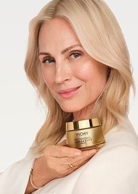 Blonde Frau hält einen goldenen Tiegel Vichy NEOVADIOL Longevity Cream