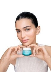 Person hält einen Cremetiegel von Vichy Mineral 89 in den Händen, trägt ein weißes Oberteil und präsentiert das Produkt vor hellem Hintergrund.