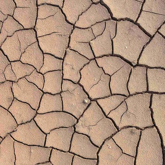 Trockene, rissige Erde in Nahaufnahme, mit unregelmäßigen Mustern, die auf Trockenheit und Wasserknappheit hinweisen.