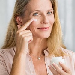 lächelnde Frau mittleren Alters trägt Creme auf ihre Wange auf