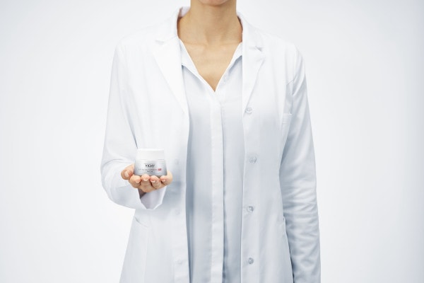Frau mit weißem Kittel hält Creme in der Hand