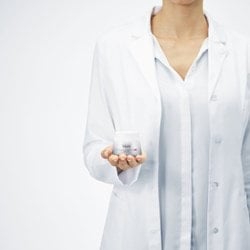 Frau mit weißem Kittel hält Creme in der Hand