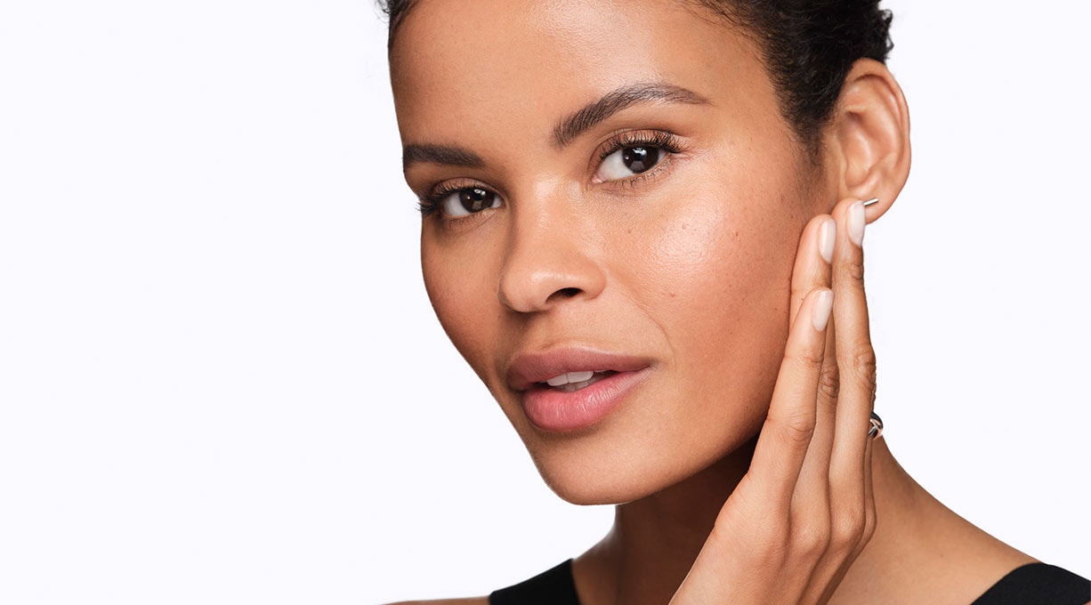 Eine gepflegte Frau sieht in die Kamera und hält eine Hand an ihre Wange