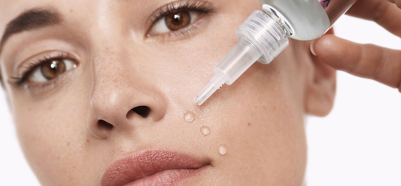Frau tropft drei Tropfen durchsichtiger Flüssigkeit in ihr Gesicht