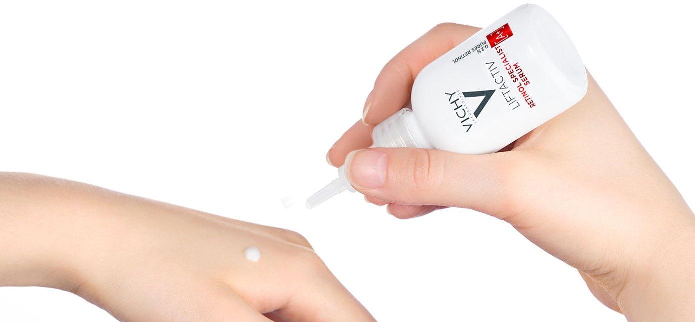 Eine Hand gibt einen Tropfen weißes Serum auf einen Handrücken