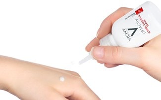 Eine Hand gibt einen Tropfen weißes Serum auf einen Handrücken