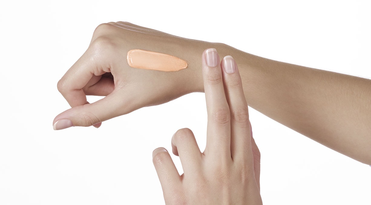 Frau trägt mit zwei Fingern Make-up auf ihre Hand auf