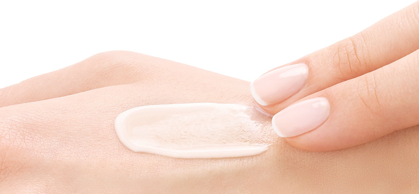 Zwei Finger verteilen Creme auf einem Handrücken