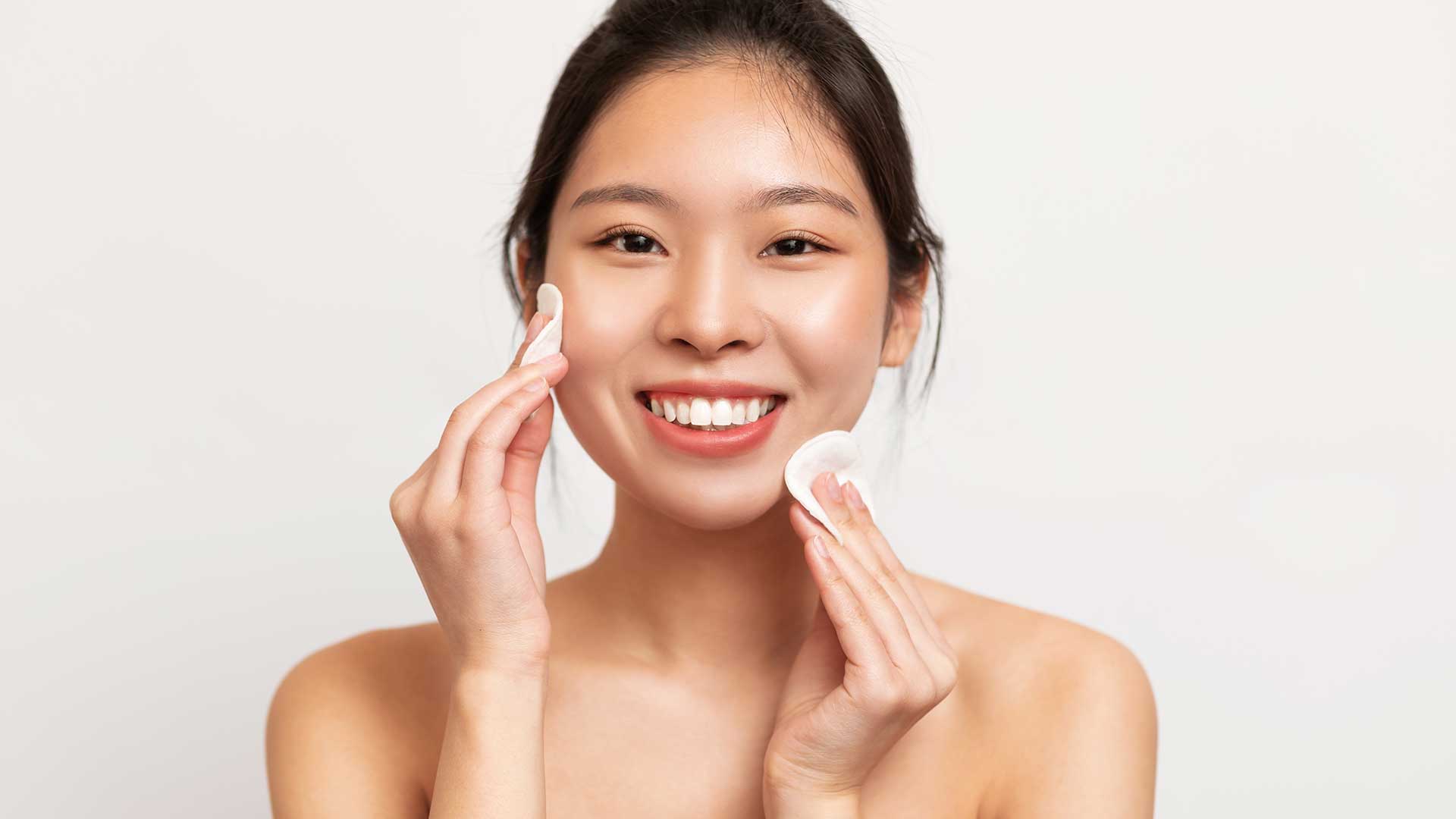 Lächelnde Frau reinigt ihr Gesicht mit zwei Wattepads