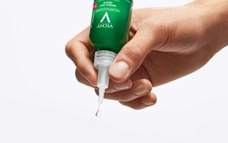 Hand drückt einen Tropfen Serum aus einer Flasche