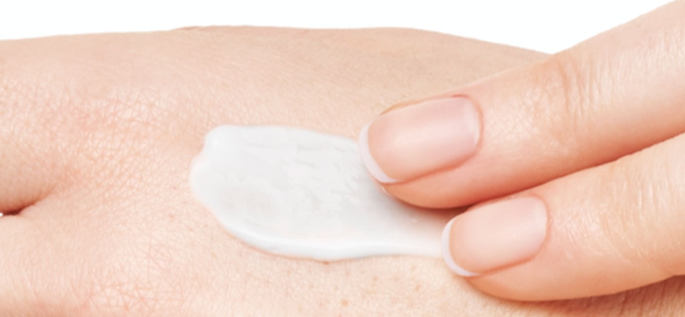Zwei Finger tragen eine weiße Creme auf trockene Haut auf