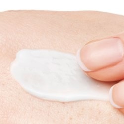 Zwei Finger tragen eine weiße Creme auf trockene Haut auf