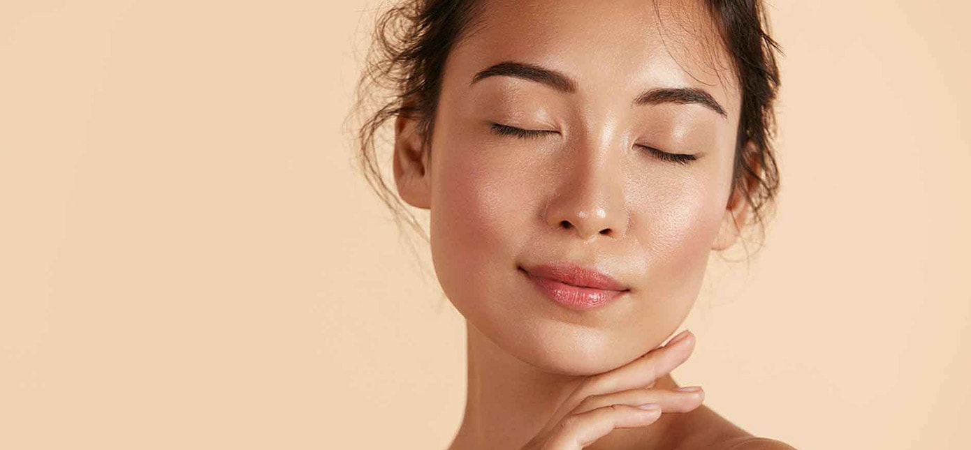 Frau mit geschlossenen Augen und glänzender Haut vor hell-orangenem Hintergrund