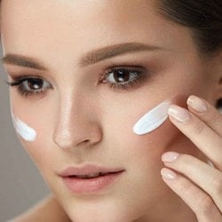 Eine pepflegte Frau verteilt weiße Creme auf ihre Wangen