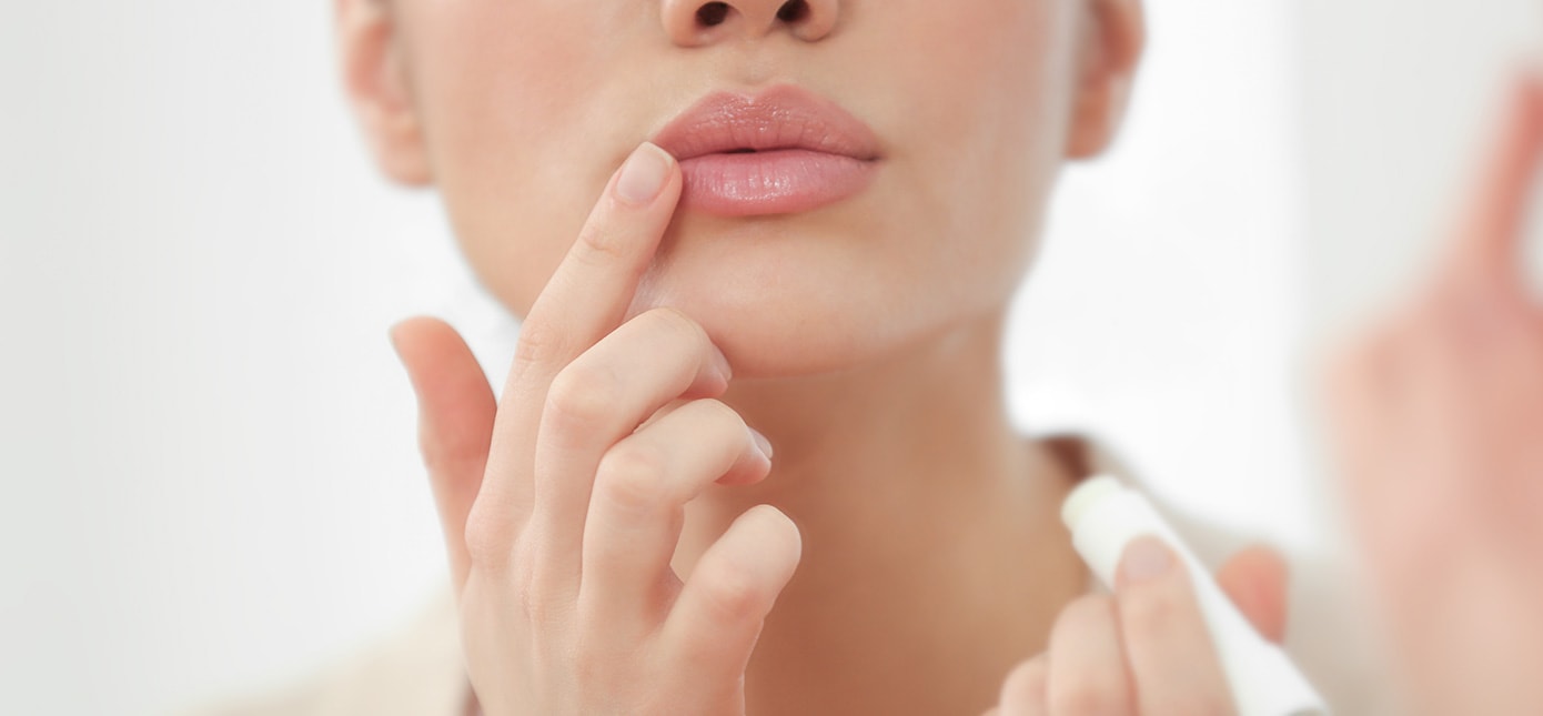 Frau trägt mit dem Zeigefinger Lippenbalsam auf