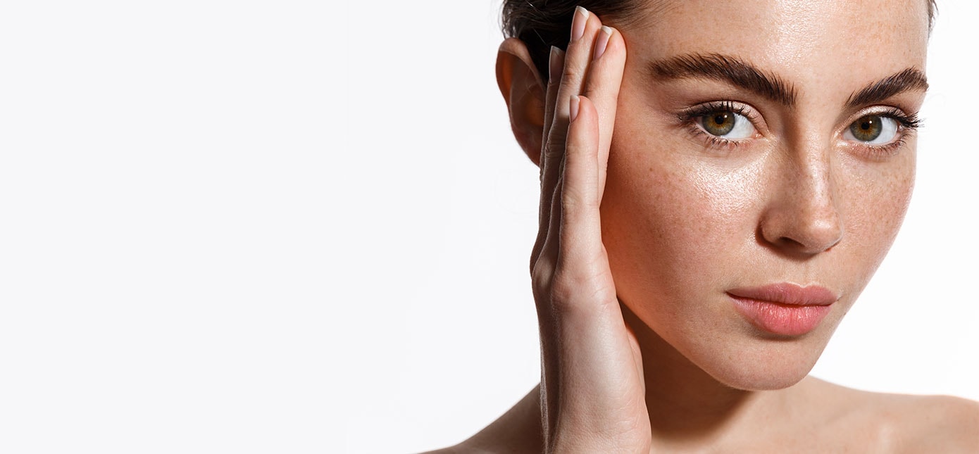 Eine junge Frau mit Sommersprossen hält eine Hand an ihr Gesicht