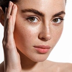 Eine junge Frau mit Sommersprossen hält eine Hand an ihr Gesicht