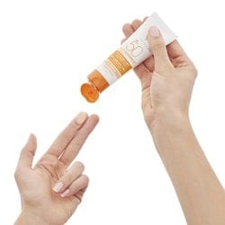 Hand gibt ein wenig getönte Sonnencreme auf einen Zeigefinger